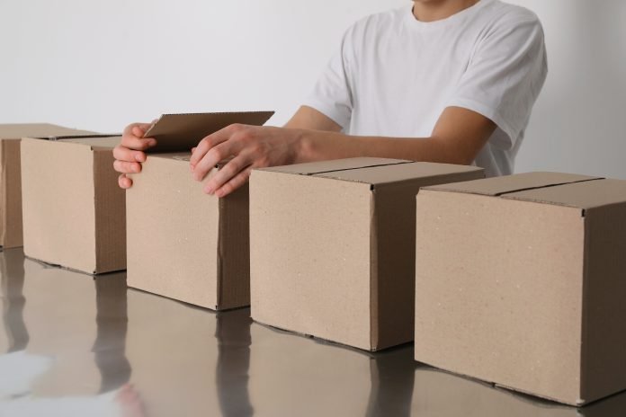 Man folding cardboard boxes at table, closeup. Production line Ansa