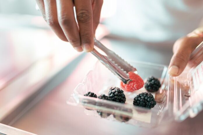 An ice-cream parlor worker is preparing some raspberry and blackberries on the roll machine using tongs GRECO