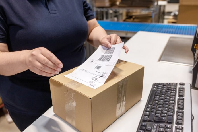 Close-up of woman worker sticking a label on a delivery box at warehouse Herma